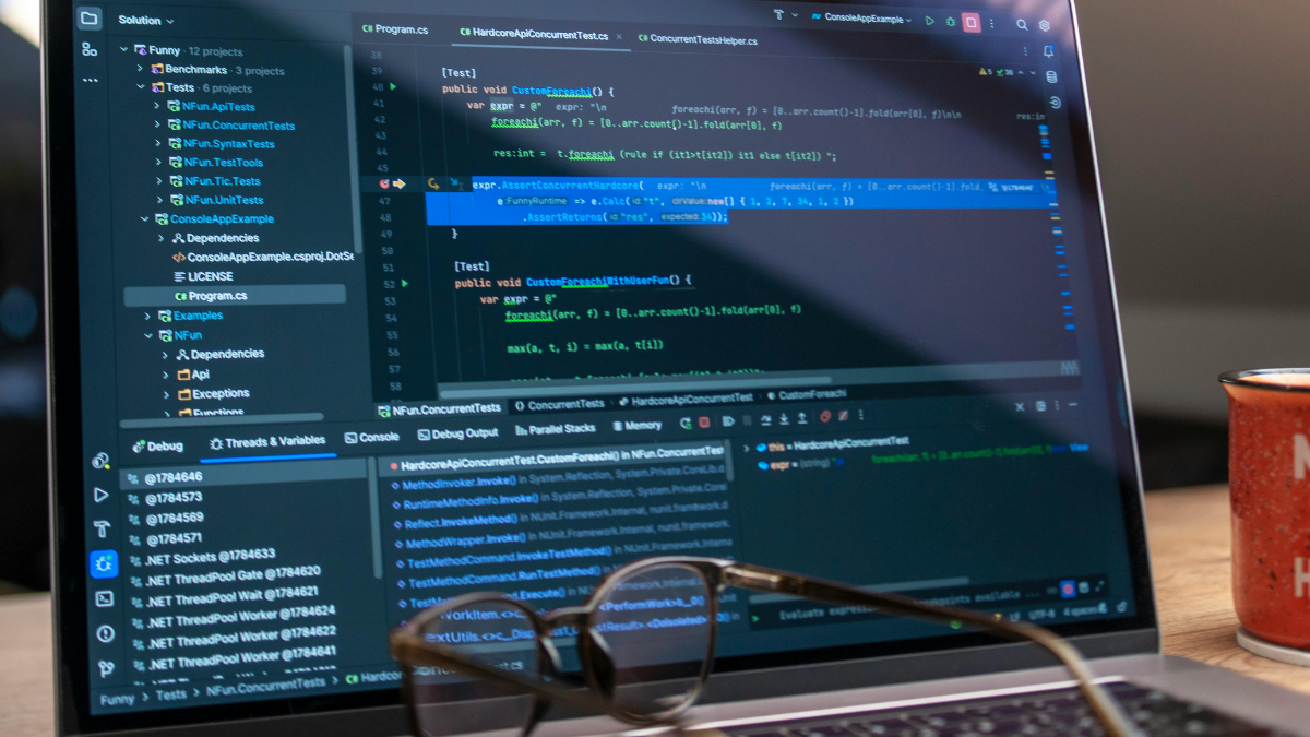 Laptop screen with Visual Studio Code editor open and programming code; a pair of glasses in the foreground and a red mug on the right.