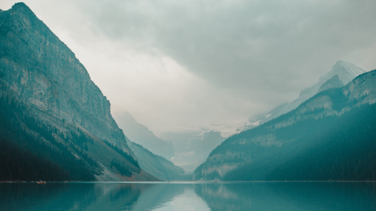 Berglandschaft mit See im Vordergrund und bewölktem Himmel.