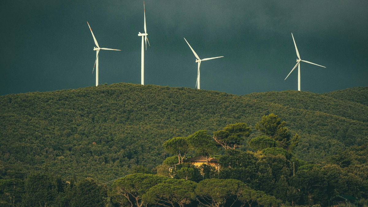 Four wind turbines on forested hills under a cloudy sky