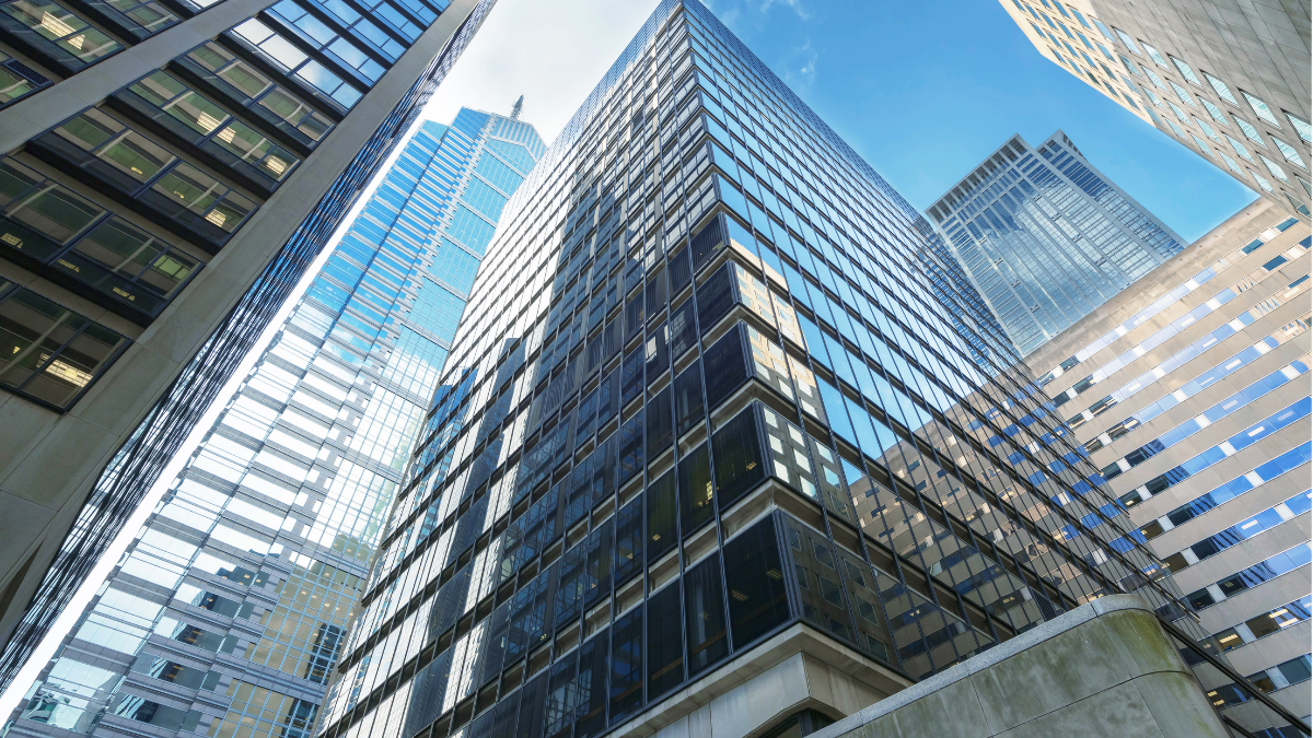 Upward view of several tall glass and steel buildings in a city under a clear sky