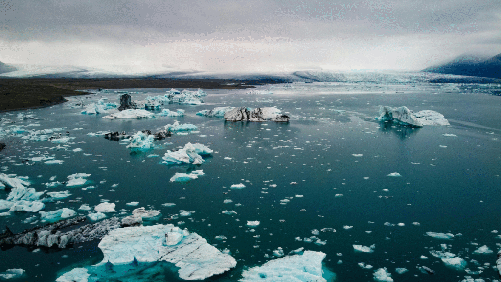 Luftaufnahme eines Gewässers mit verstreuten Eisbergen und bewölktem Himmel