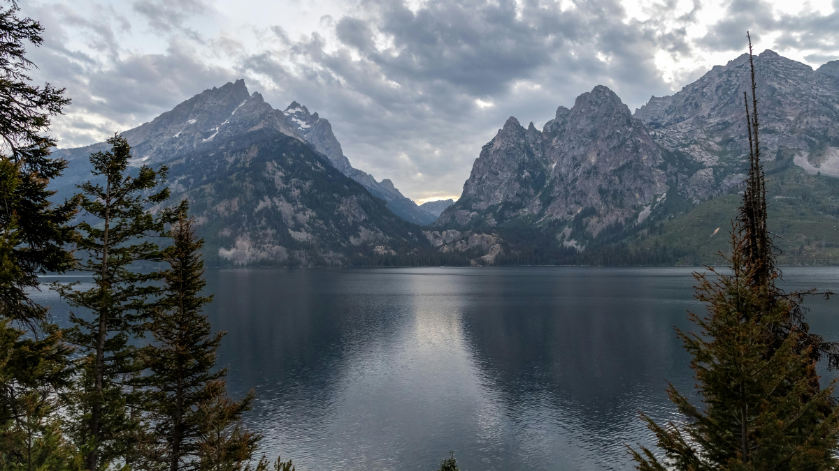 Mountain lake with a reflective water surface surrounded by coniferous trees and high mountains under a cloudy sky